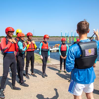a class of young sailors wearing helmets and life jackets listening to an instructor