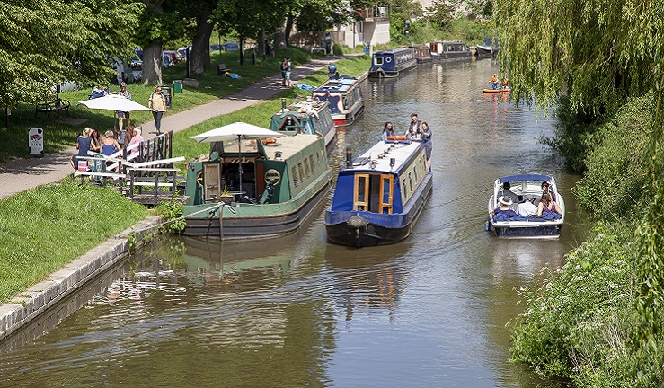 A canal boat is travelling past a motor boat on a river.