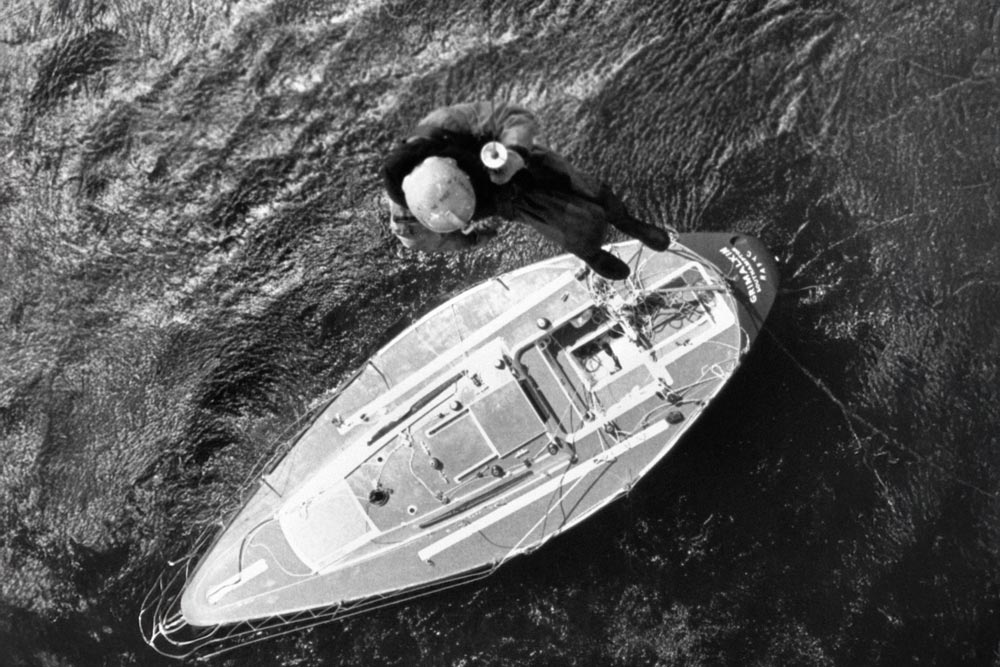 A helicopter crewman hangs from a winch to check the battered yacht Grimalkin for possible survivors in the wake of the Fastnet race disaster. 15 August 1979