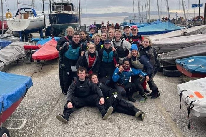Group picture of members of Durham University Sailing Club taken on shore in a boat park.
