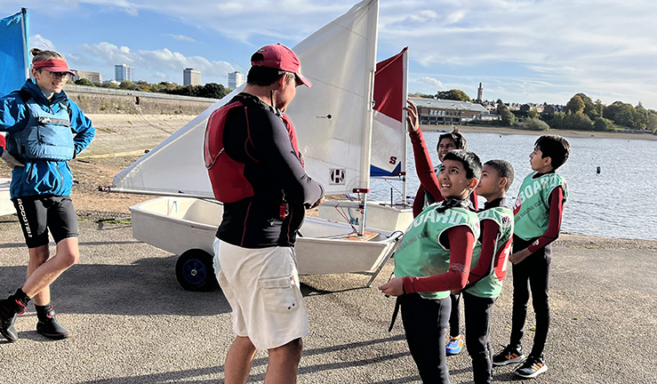 OnBoard instructor chatting to junior sailors on shore by a lake.