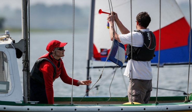 Two people on a committee boat making flag and sound signals for racing.