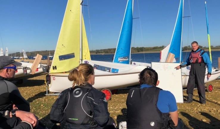 Group of sailors on shore listening to an instructor on a race coach course.