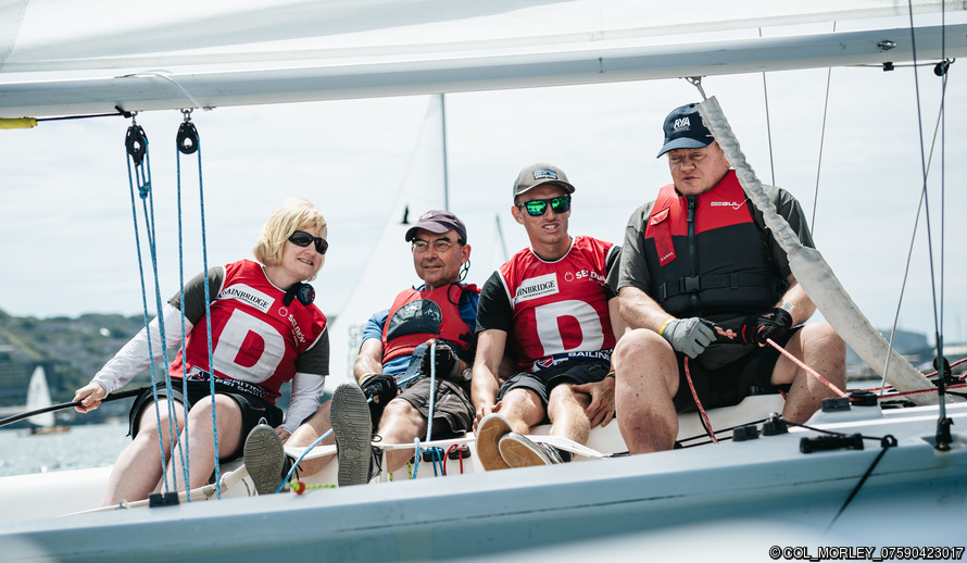 Blind Sailing team members racing a keelboat, sitting in the side. 3 visually impaired people sailing with one sighted crew.
