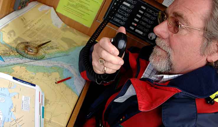 Yacht towing a yacht and man on radio at chart table on yacht