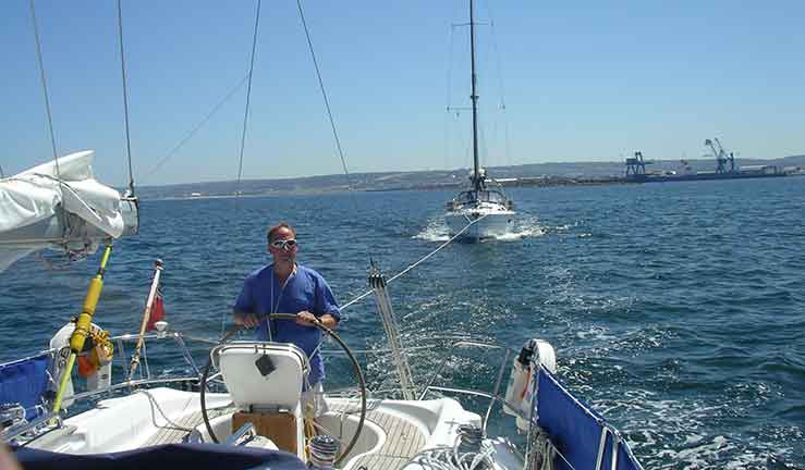 Yacht towing a yacht and man on radio at chart table on yacht