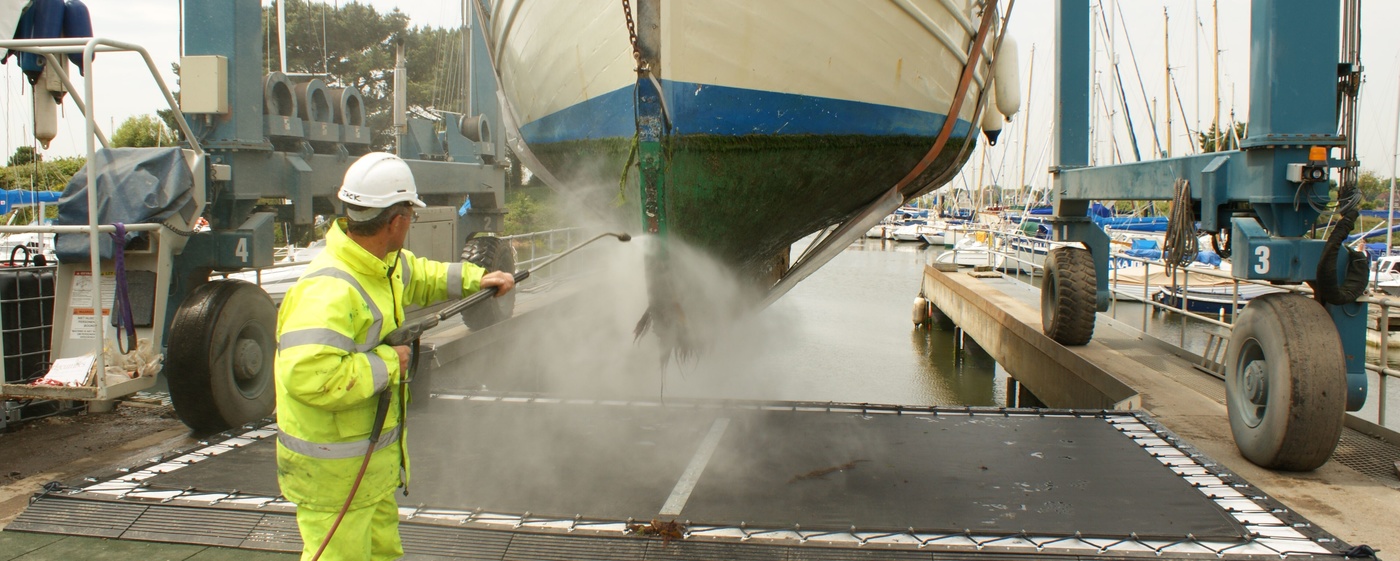 Man in high vis power washing the hull of a boat.