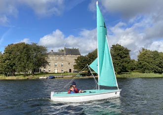 A Hansa sailing dinghy passes a Castle as part of a disability Sailing Open Day