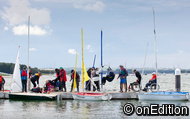 A busy pontoon with boats moored alongside, people being hoisted into  boats, people in wheelchairs waiting to get into boats, and general excitement about going sailing.