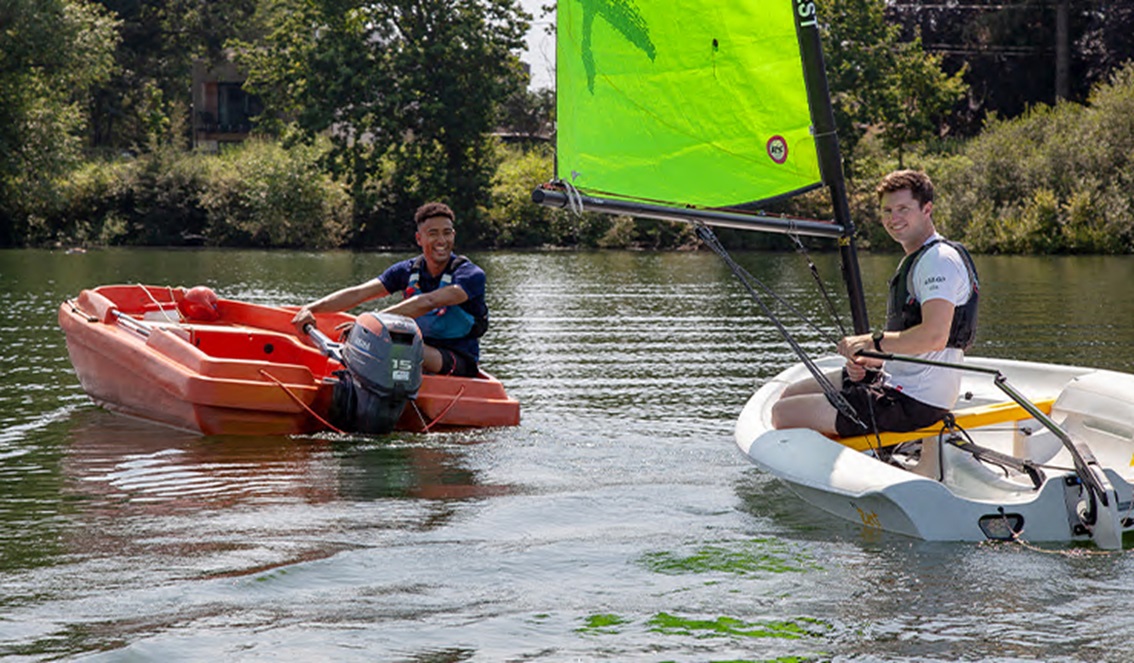 Wide shot of two teenagers sailing boats on a lake