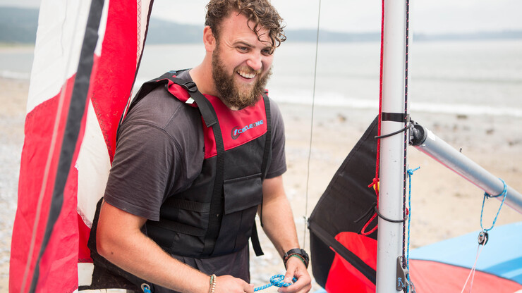 Man rigging a dinghy and laughing with friends