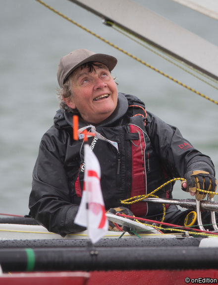A sailor watching the sail carefully, controlling the mainsail and smiling despite the rain