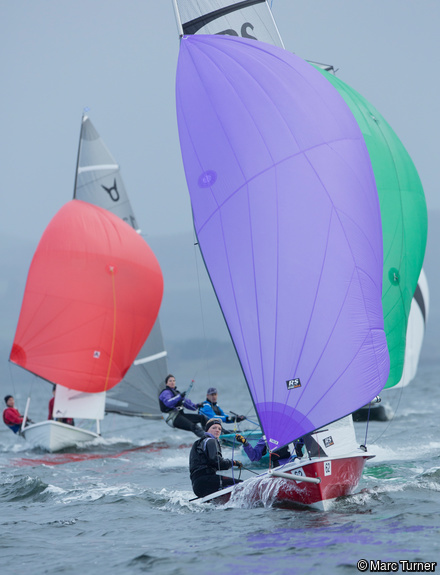 Colourful sails in a fleet of dinghies racing downwind.