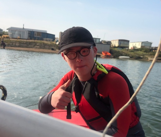 Alex in his sailing boat, smiling at the camera with his thumb up