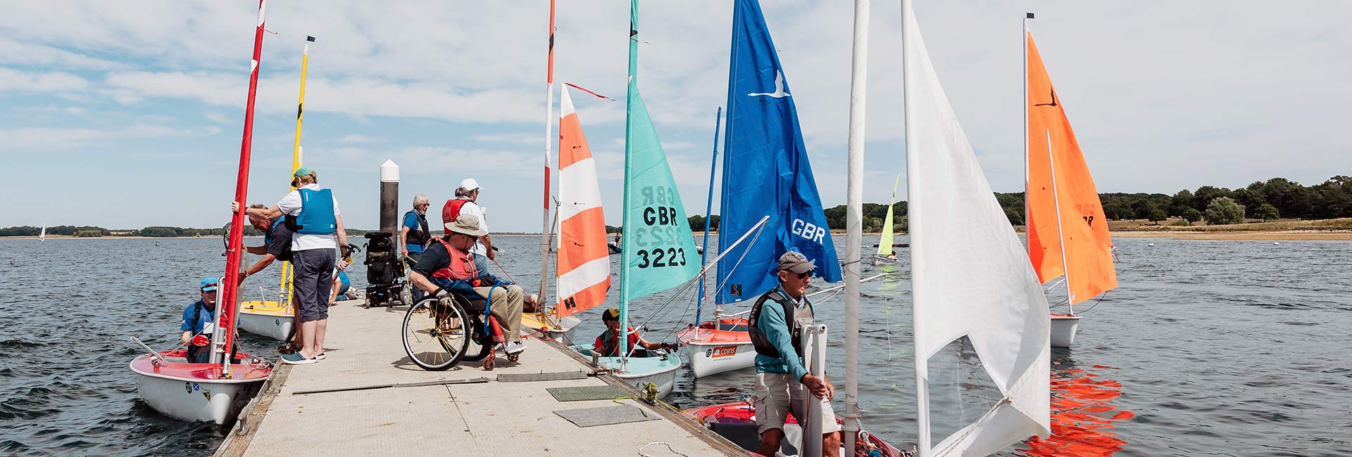 Wide shot of people climbing into moored sailing dinghies  