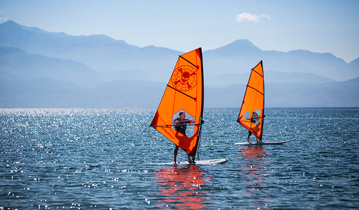 wide shot of two people windsurfing on a very calm lake