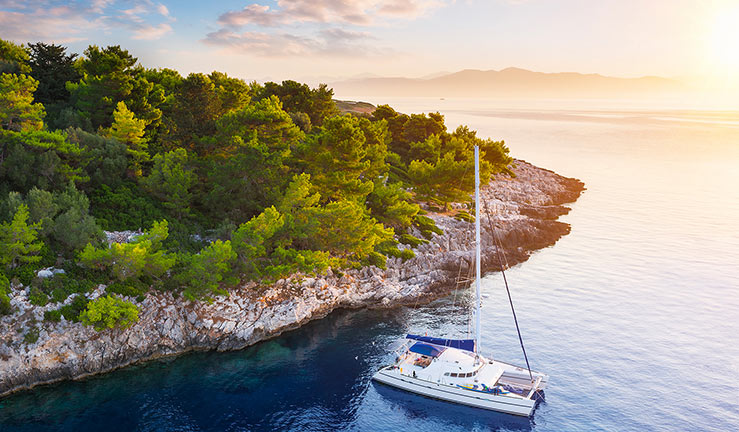 wide shot of sailing yacht next to an island during sunset