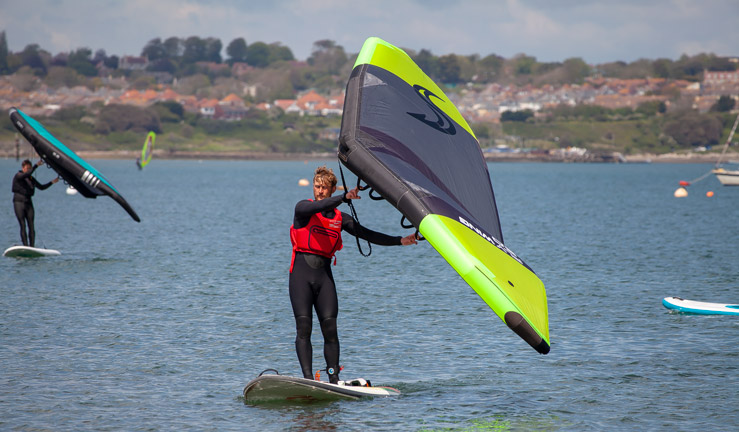 RYA learn to wingsurf course - man learning to wing. Other wingsurfers in background.