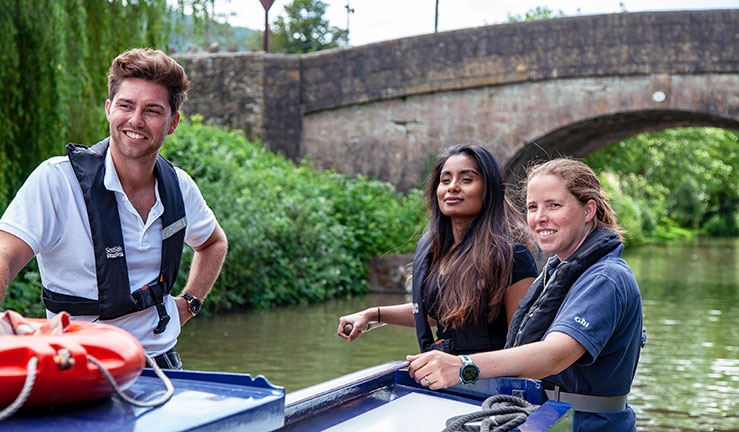 mid shot of three people on a canal boat, it's a beautiful day