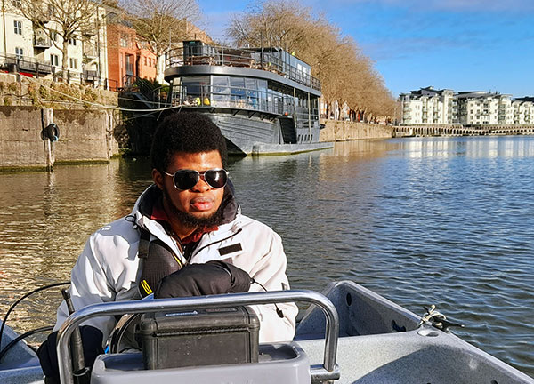 Mid-shot of young man wearing sun glasses driving motor boat on city river on a sunny day