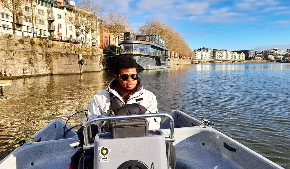 mid-shot of young man driving motorboat on a city river on sunny day