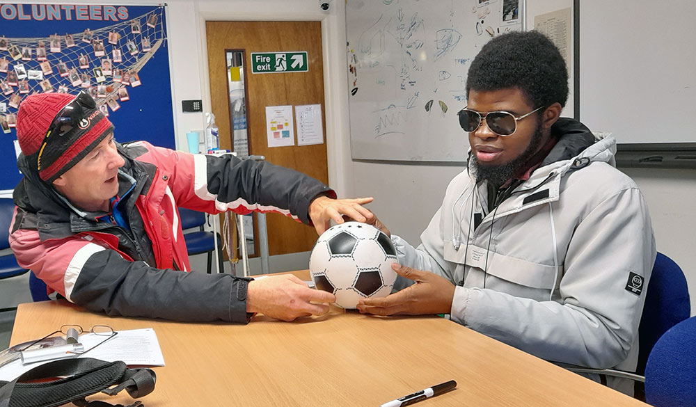 instructor demonstrating something to young man using a football as a an educational prop 