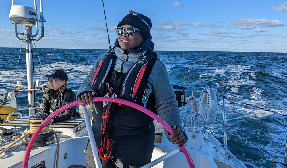 smiling woman wearing shades while steering large yacht on the open water