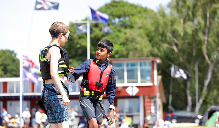 midshot of two children walking and talking in foreground of sailing club