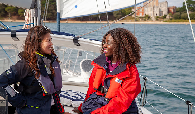 mid-shot of two young women having a conversation on yacht while smiling