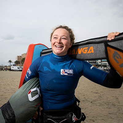 mid shot of smiling kite surfer standing on a sandy beach 