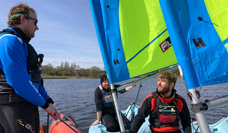 Dinghy instructor talking to two sailors on a lake