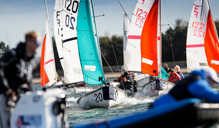 wide shot of a fleet of smiling sailing in dinghies