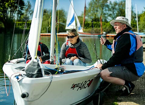 volunteer talking to two sailor in a sailing dinghy on a lake