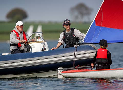 sailing instructor sitting in a motorboat talking to child in a sailing dinghy