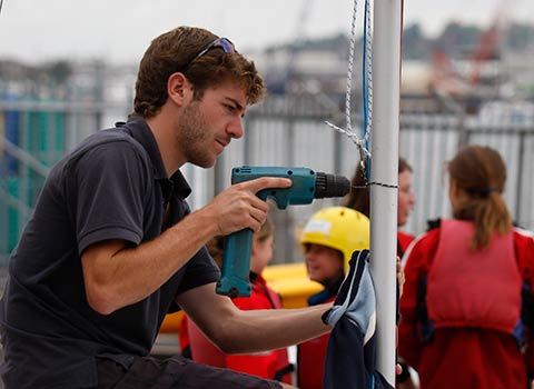 young man fixing dinghy boat using electric drill