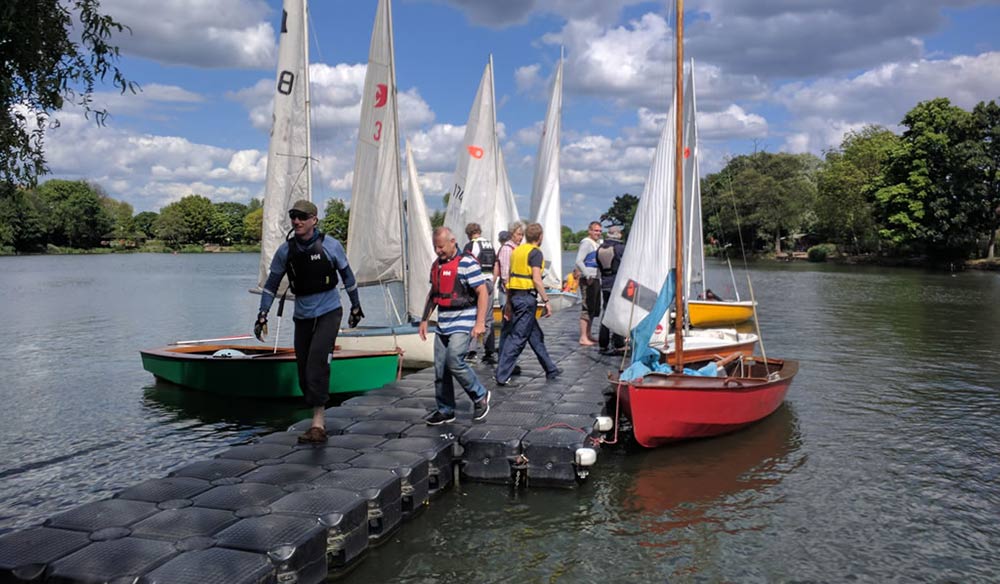 6 classic sailing dinghies moored on a lake surrounded by people 