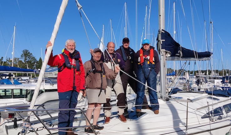 5 people smiling standing on a yacht.
