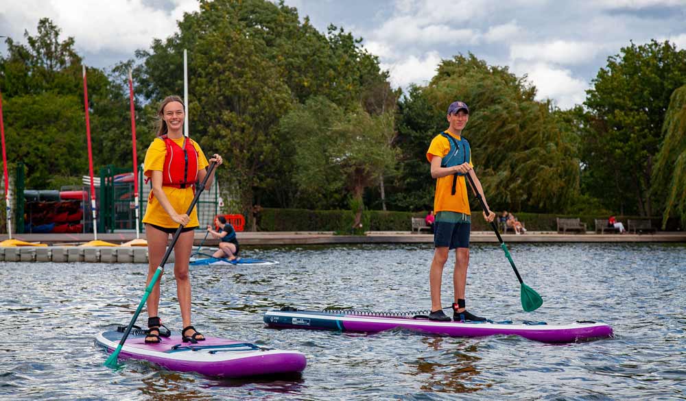 two young people paddleboarding with safety equipment 