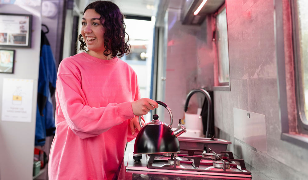  woman boiling a kettle on a gas cooker in boat 