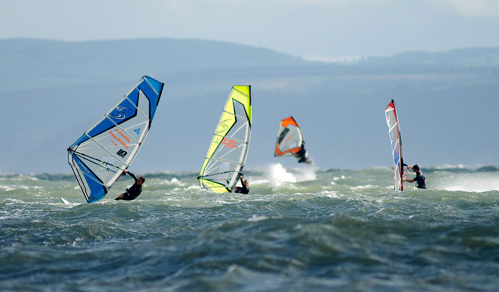 Wide shot of 4 windsurfers in the distances 