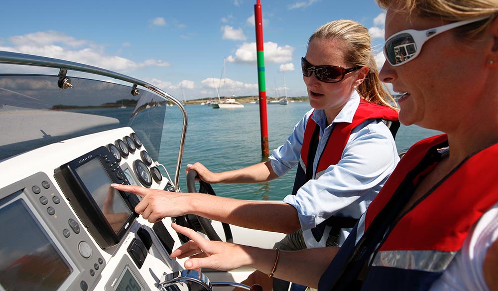 Wide shot of two women steering and navigating a boat
