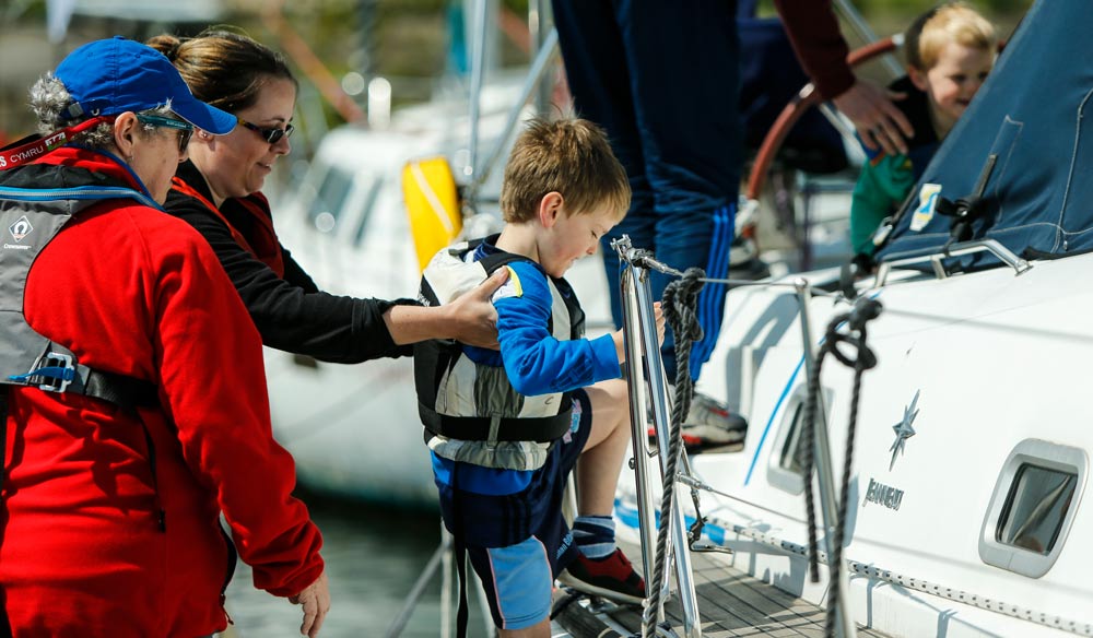 wide shot of child being helped onto boat by mum