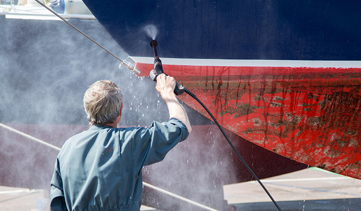 close up of man spraying down bottom of boat to remove barnacles and unwanted stuff