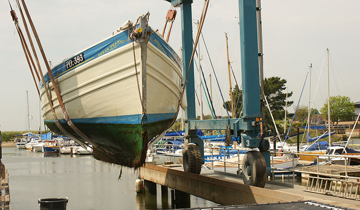 wide shot of boat being hoisted out of the water that needs antifouling