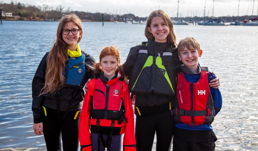 Group shot of 4 children on beach wearing buoyancy aids and lifejackets