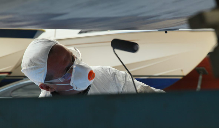 Wide shot of man painting boat with antifoul paints