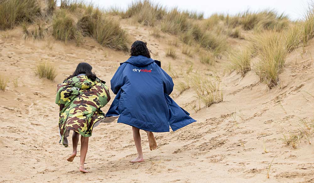 2 kids running up sand dune in dryrobes