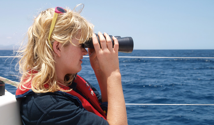 wide shot of woman on boat using binoculars