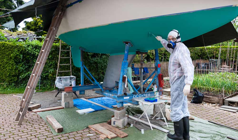 boat being painted and paint drops being collected by tarp