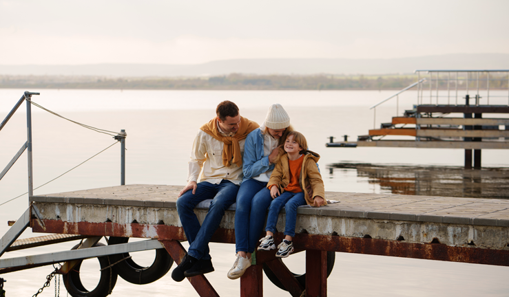 a mother, father and son sitting on a dock 